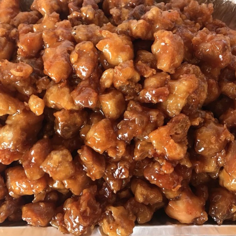 Close-up of glistening, golden-brown General Tso's chicken pieces in a silver serving tray.