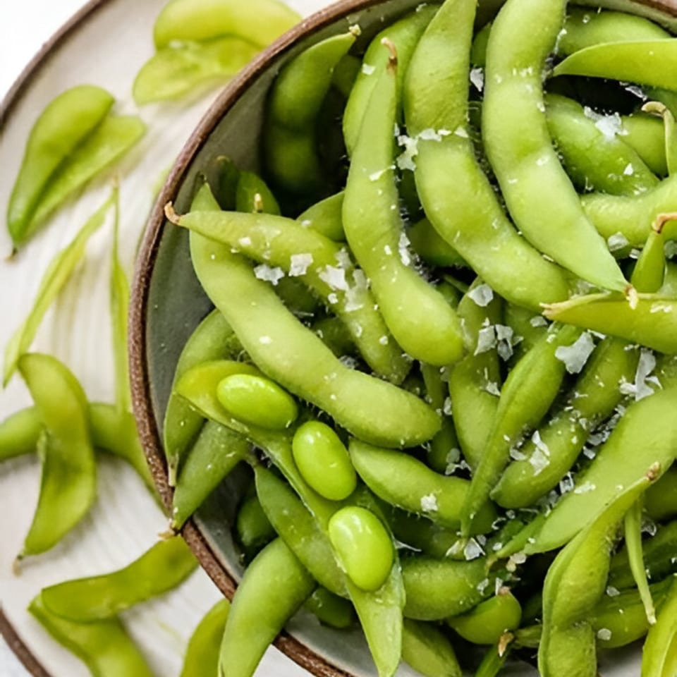 A bowl of vibrant green edamame pods, some shelled, sprinkled with sea salt.