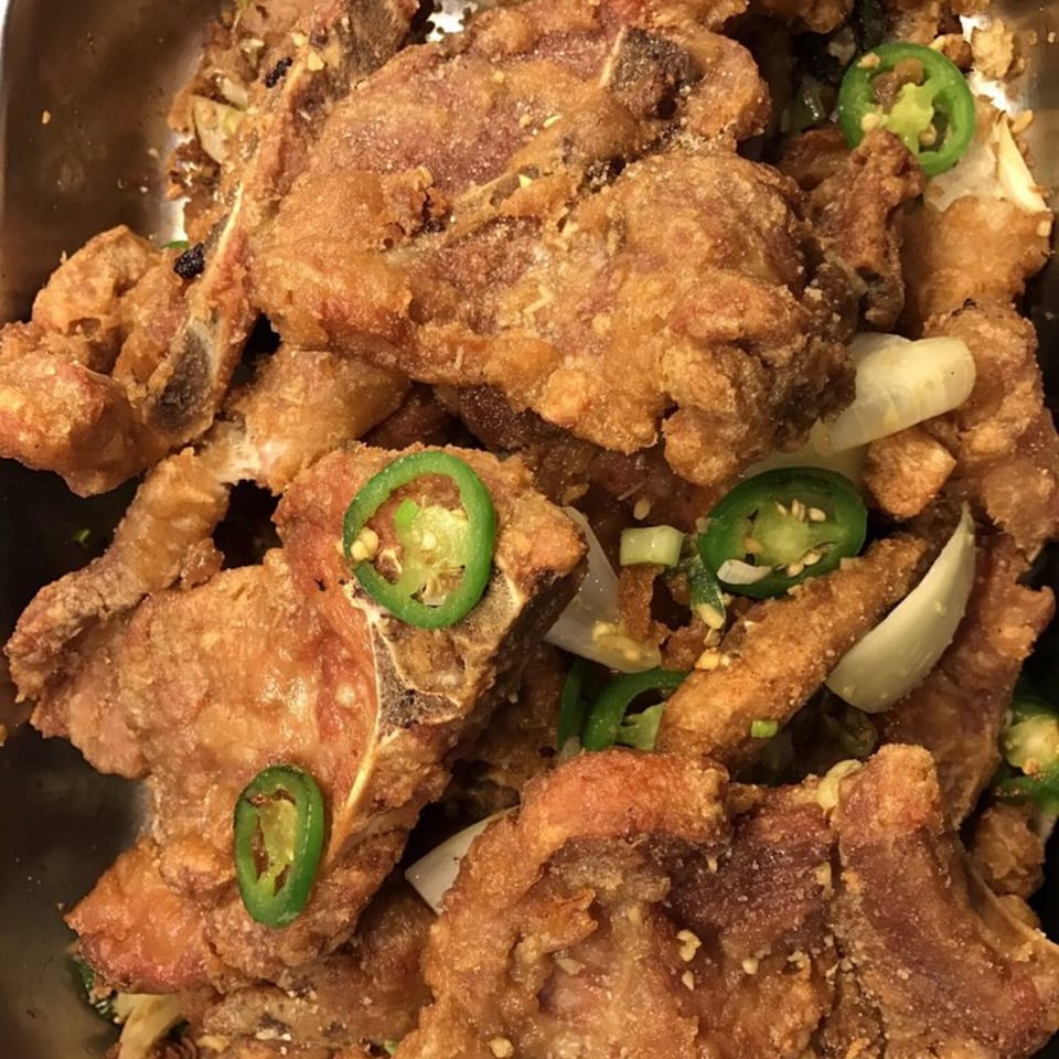 Close-up of crispy fried pork chops with sliced green chilies and onions.