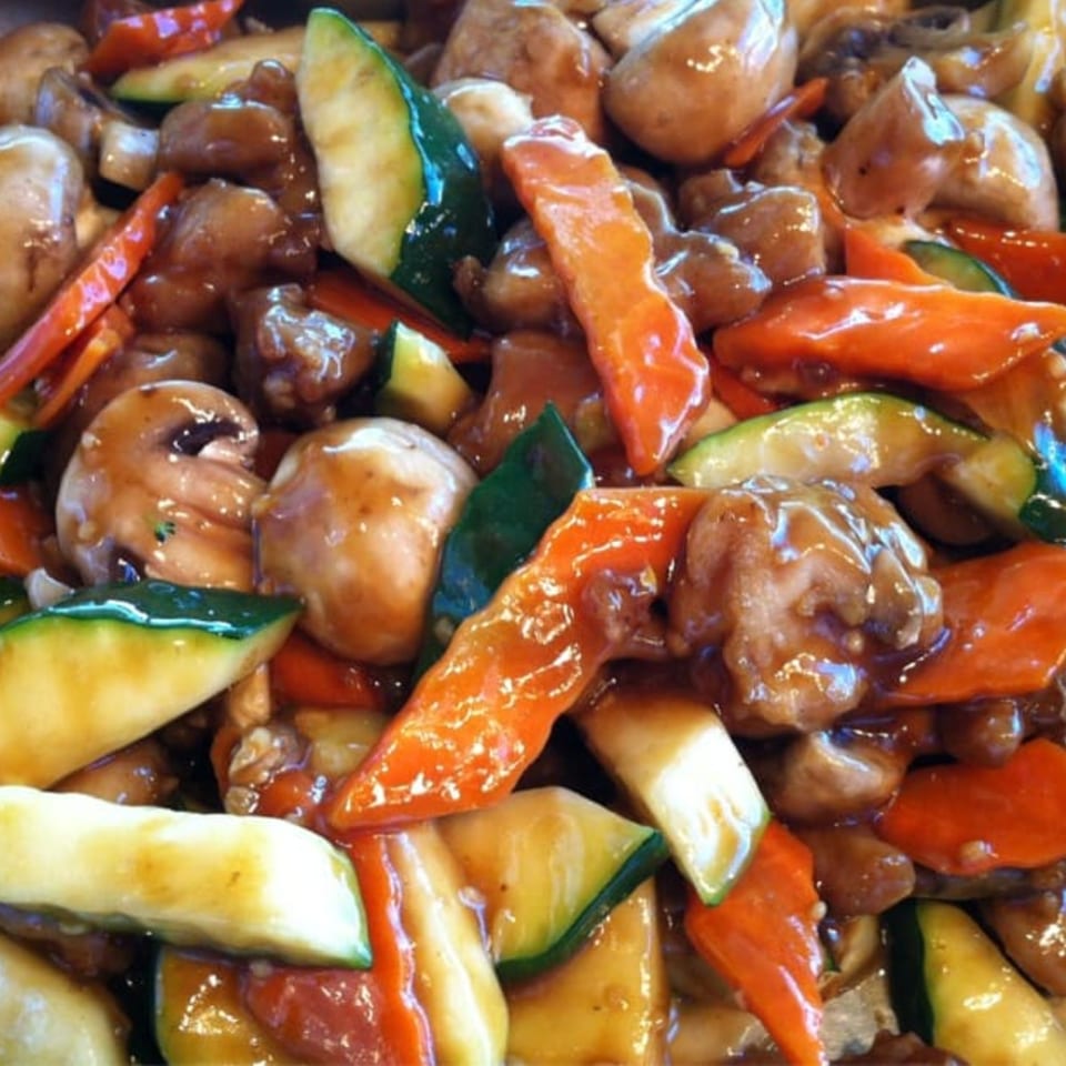 Close-up of Chinese stir-fry with chicken, mushrooms, zucchini, and carrots in a glossy sauce.